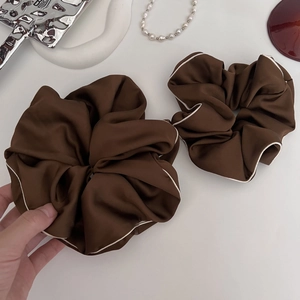 Close-up of two large dark brown satin hair scrunchies with white contrast piping detail