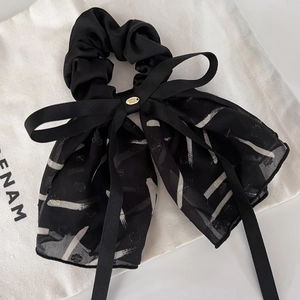 Detail of printed black bow hair scrunchie with long ribbons and gold metal tag