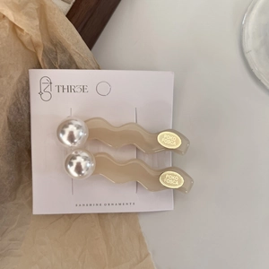Close-up of wavy cream hair clips with faux pearls and gold seals on display card