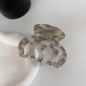 Detailed macro view of acetate hair claw clip with grey tortoiseshell pattern and gold logo