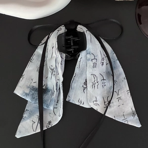 Detail of white fabric bow hair clip with black ink painting print and flowing ribbons
