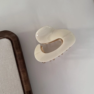 Detail of a minimalist cream white acetate hair claw with gold metal spring mechanism
