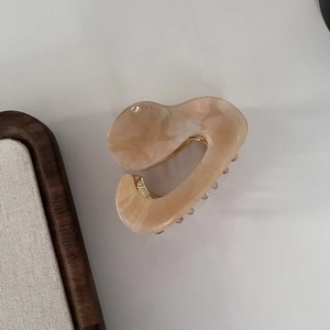 Detail showing irregular acetate hair claw clip with peach pearlescent texture and gold spring