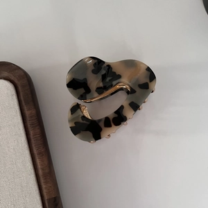 Detail view of acetate hair claw clip with tortoiseshell pattern and golden metal hinge