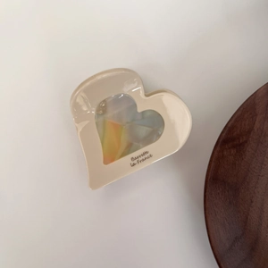 Détail d'une pince à cheveux cœur crème avec résine irisée et inscription logo gravée