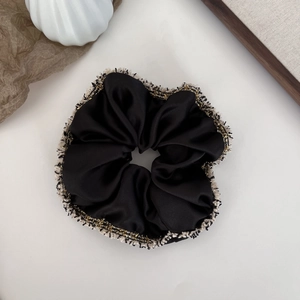 Détail d'un chouchou en satin noir avec bordure en tweed dorée et beige sur fond blanc