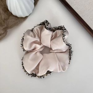 Détail du chouchou en satin champagne avec bordure en tweed élégante et fil doré brillant