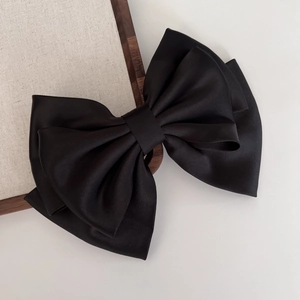 Macro shot of large black satin bow hair clip with high-end texture and elegant draping