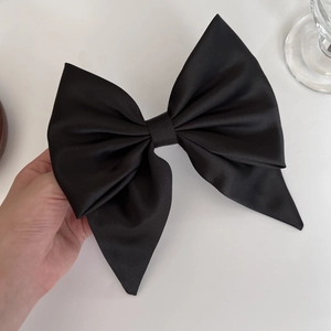 Close-up of a large black satin bow hair clip with smooth silk texture and soft sheen