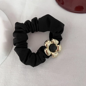 Dettaglio di un elastico nero per capelli con fiore in metallo dorato su tessuto bianco