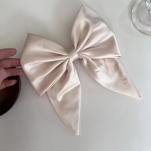 Macro detail of the smooth champagne satin fabric texture and bow design of this hair clip
