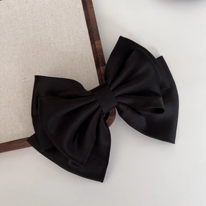 Macro shot of large black satin bow hair clip texture on a neutral linen backdrop
