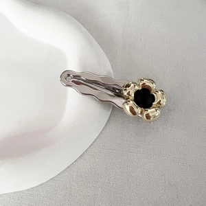 Dettaglio di un fermaglio per capelli argento con fiore dorato su ceramica bianca sagomata