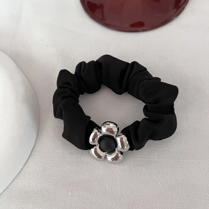 Dettaglio di un elastico scrunchie nero con ciondolo floreale in metallo argento