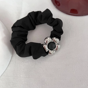 Elegante elastico per capelli nero con fiore in metallo su sfondo di tessuto bianco