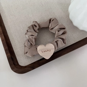 Detailed shot of champagne satin scrunchie with Lucky heart charm on a linen background