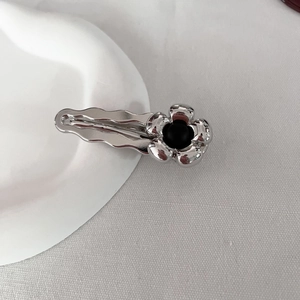 Dettaglio di un fermaglio per capelli a fiore argento con centro nero su piatto bianco
