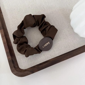 Detail of dark coffee satin scrunchie with Lucky engraved gold buckle on gray linen