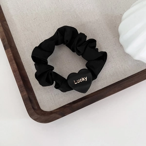 Detail of black satin scrunchie featuring a matte heart charm with golden Lucky text