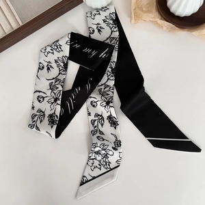Detail of a black and white floral silk twilly scarf styled on a minimal white surface