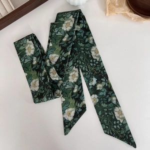 Detailed view of dark green floral silk twilly scarf laid flat on a rustic background