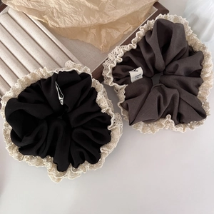 Detailed view of black and brown lace-edged hair scrunchies on a textured display base