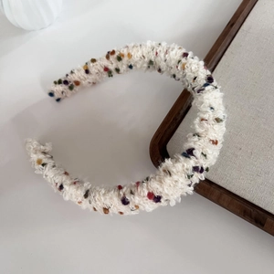 Close-up of a white knit headband with colorful plush pom-poms and soft wool texture