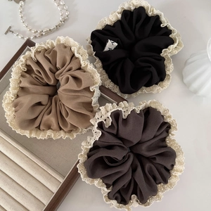 Detailed view of French lace scrunchies in khaki, black and dark coffee on a chic tray
