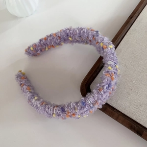 Detailed texture of purple knit headband with orange and yellow pom-poms on wooden tray