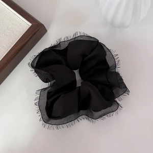 Détail d'un chouchou en satin noir avec bords effilochés et pompons sur fond blanc