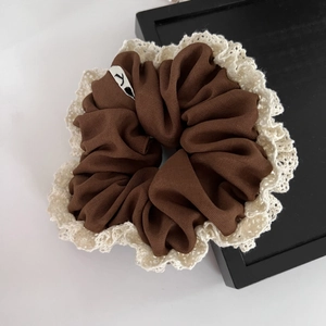 Close-up of brown scrunchie with white lace trim and small logo tag detail
