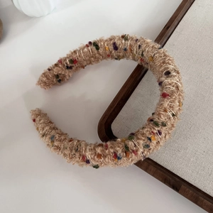 Close-up of khaki boucle knit headband with colorful dots and metallic thread detail