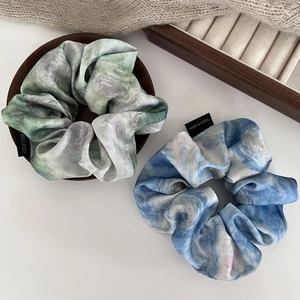 Detail of two satin scrunchies featuring oil painting textures in blue and green hues