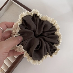 Close-up of brown satin scrunchie with cream lace trim held over a wooden jewelry box