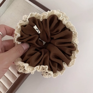 Detail of dark brown scrunchie with beige lace edges and a small white letter Y tag