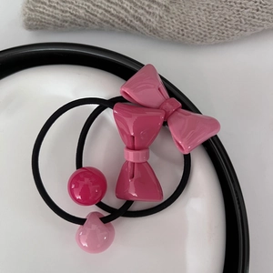 Zwei elastische Haargummis mit rosa Schleifen und Perlen auf einem Keramikteller