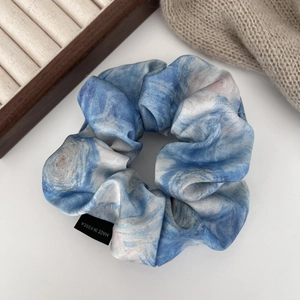 Close-up of blue and white watercolor silk scrunchie with detailed stitching and soft texture