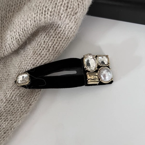 Detailed close-up of black velvet hair clip with rhinestones, pearl, and gold hardware