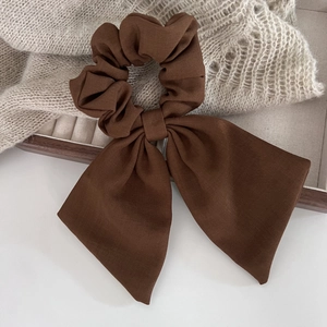 Détail d'un chouchou marron foncé avec de longs rubans sur un tissu en maille texturé