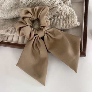 Chouchou élégant avec nœud marron en tissu texturé disposé sur un plateau en bois