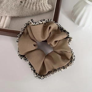 Detailed close-up of brown scrunchie with fringe edges on a wooden tray background