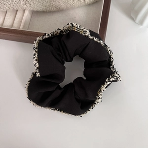 Detailed view of the black tweed hair scrunchie with gold threads and white fringe edges
