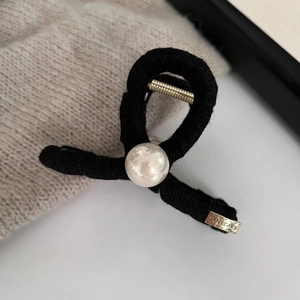Close-up of black knitted fabric hair claw clip with a glossy white pearl and golden spring