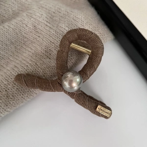 Close-up of pearl hair claw clip with wool wrap texture and golden brand plate