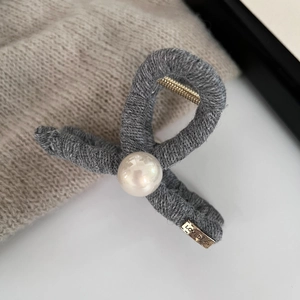 Detailed close-up of dark grey knitted hair claw clip with pearl and gold metal logo