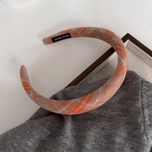 Detailed view of handmade plaid headband with orange fabric texture and woven label