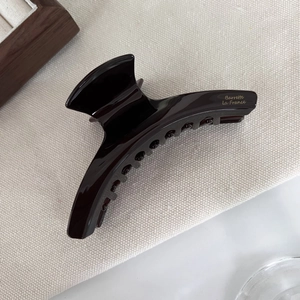 Detail of dark brown acetate hair claw clip with smooth glossy finish on beige fabric