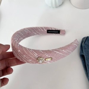 Detailed macro view of pink tweed headband with camellia pearl charm and metallic logo tag