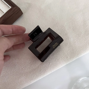 Detailed view of the dark brown tortoiseshell acetate hair claw with golden lettering