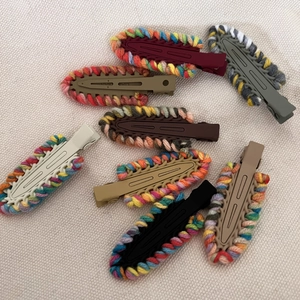 Close-up of seven colorful knitted yarn crochet hair clips on a soft textured background